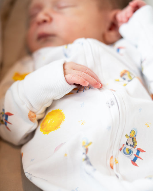 Newborn baby wearing Pima Bee's Elvis the Astro Turtle Zippy featuring colorful space-themed designs.